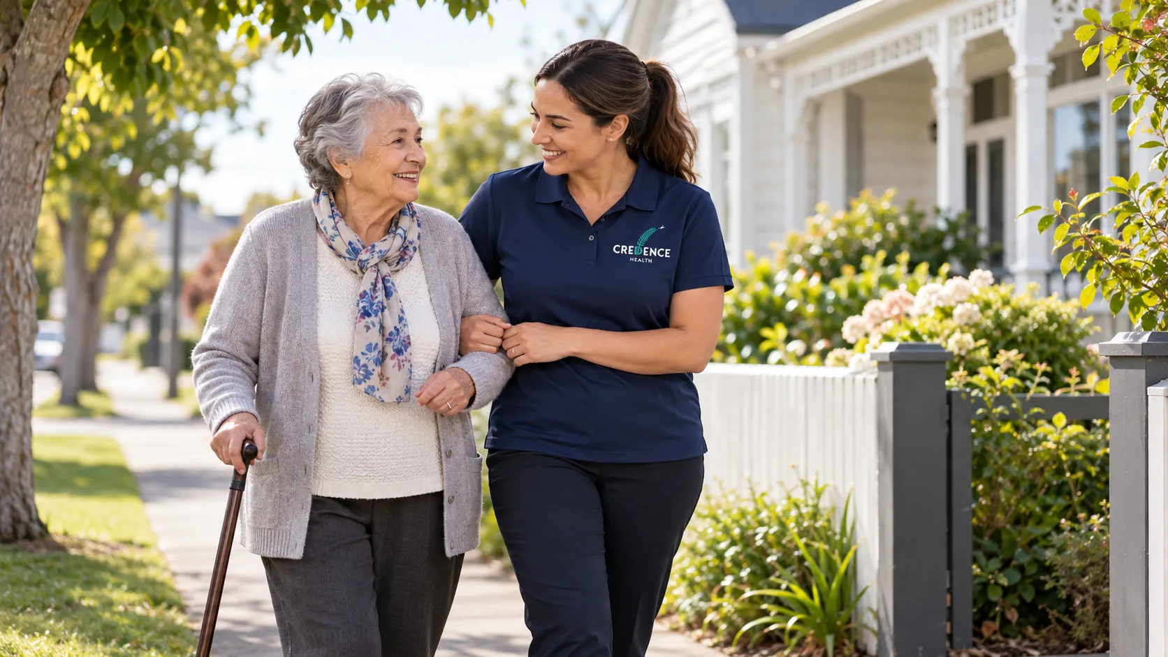 An older woman with a walking stick walking arm in arm with a home care worker